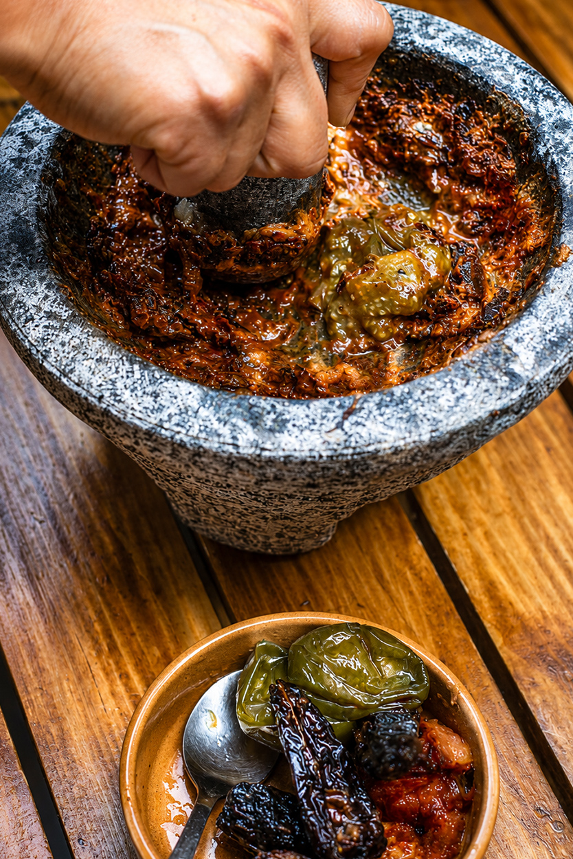 Preparación artesanal de salsa mexicana con chiles asados en molcajete de piedra.