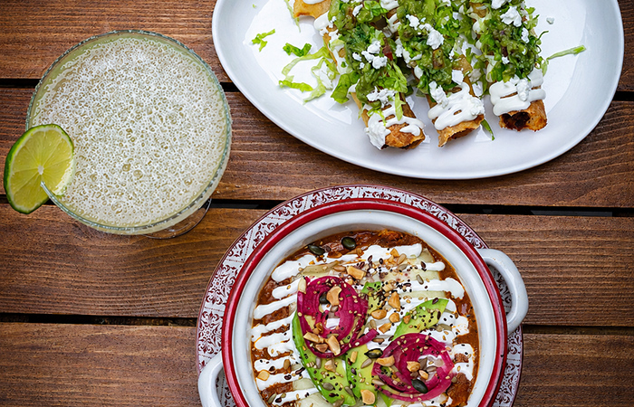 Platos de comida mexicana con, salsas y bebida con lima sobre una mesa de madera.