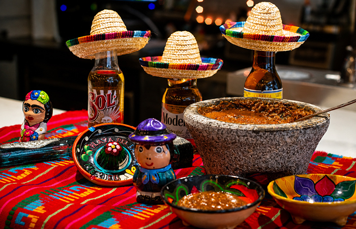 Salsas mexicanas servidas en molcajete con decoración tradicional, sombreros y elementos coloridos.
