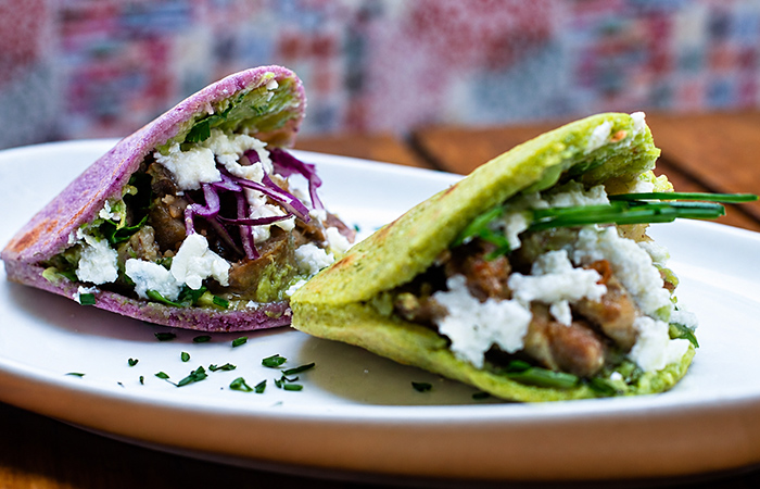 Tacos mexicanos con tortillas de colores, carne, queso fresco y verduras servidos en un plato blanco.