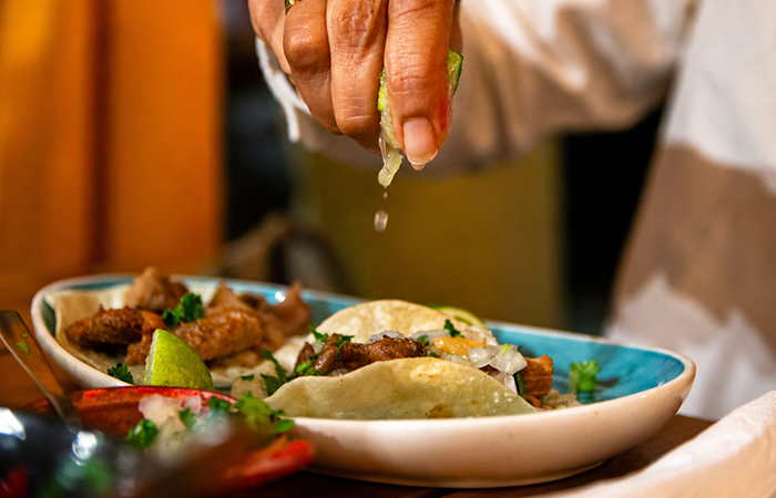 Tacos mexicanos servidos en un plato con una mano exprimiendo lima sobre ellos.