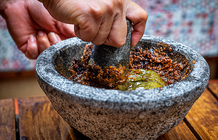 Salsa mexicana en molcajete Preparación de salsa mexicana en molcajete de piedra con chile, especias y aceite.